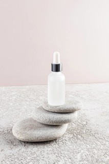 A minimalist scene of a frosted glass dropper bottle placed on smooth, stacked stones The neutral