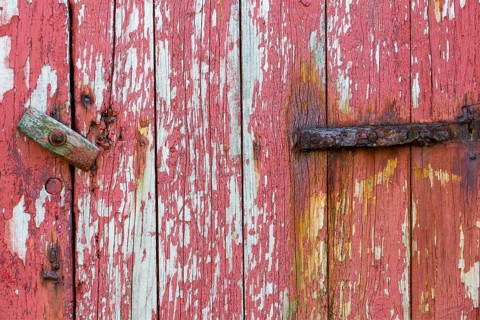 An old wooden door with peeling red paint and a rusty hinge, Mykines, Faroe Islands