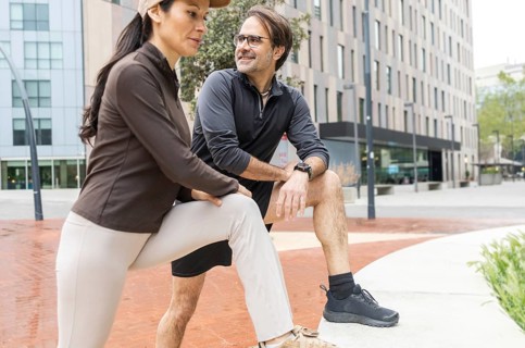 A couple engages in a stretching routine outdoors, preparing for a workout. The urban setting
