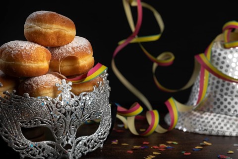 Doughnuts against a dark background next to a silver hat, carnival mask and paper snakes