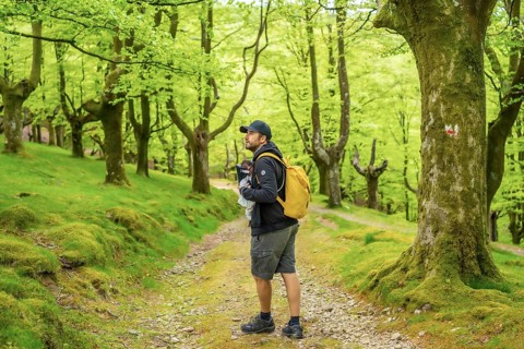 A young father walking with the newborn child in the backpack on a path in the woods heading to the