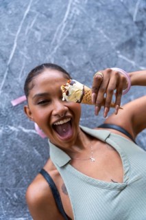 Joyful woman with a wide open mouth laughs while holding a delicious vanilla ice cream cone with