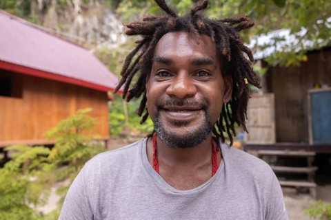 A cheerful native man with dreadlocks in front of a traditional house on Kri Island in the Raja