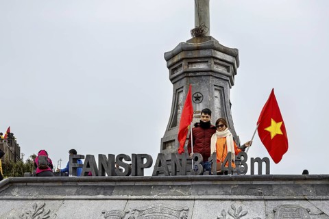 Couple holding a Vietnamese flag on a platform at Fansipan peak, surrounded by fog, The summit of