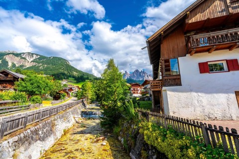 Scenic view of santa maddalena village and the odle mountains reflecting in a river during a sunny