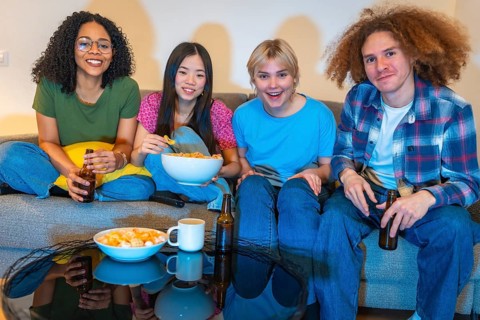 Four friends relaxing on a couch, sharing snacks and drinks while enjoying a movie together in a