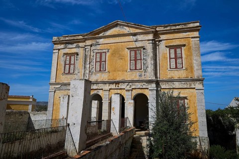 Dilapidated building with ornate windows and shades of yellow, under a bright blue sky, Symi Town,