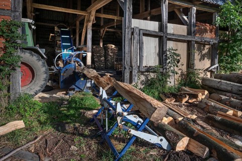 Young man sawing and splitting beech logs with his saw cutting machine, powered by a tractor in a
