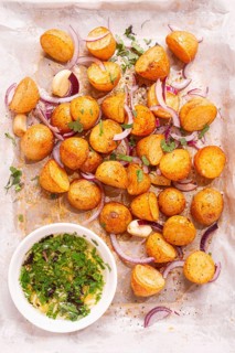 Roasted potatoes sit on a baking sheet next to chopped herbs and red onions. They are golden brown