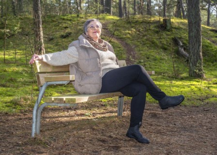 Elderly woman, 65 years old, sitting on a bench and enjoying nature in the forest in Ystad, Skåne,