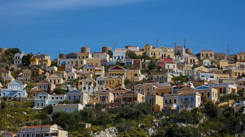 Colourful houses on a hill overlooking the sea under a bright blue sky, Symi Town, Symi,