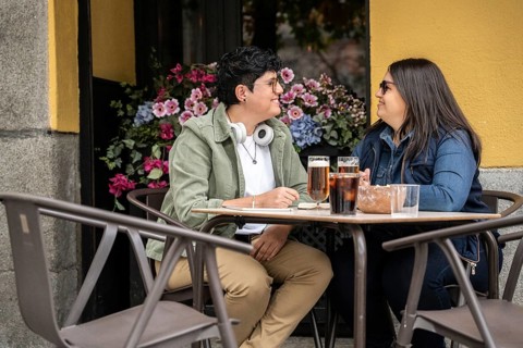 A curvy lesbian couple shares a joyful moment at an outdoor beer. They are sitting at a table with