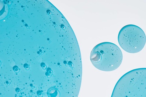 Close-up shot of blue cosmetic gel droplets with intricate texture on a white background. The image