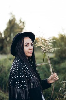 A woman with braided hair and a hat enjoys a tranquil sunset in a natural setting, holding a