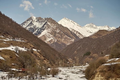 Majestic Caucasus snowy mountain peaks tower over a tranquil valley, where a rustic cabin nestled