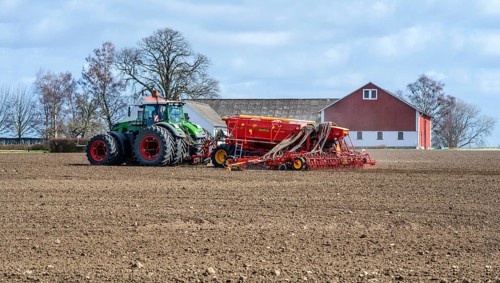 Farming, sowing with tractor in springtime and with a farm building in the background in Skurup