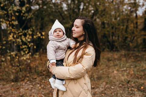 A mother holds her child during a peaceful autumn walk through a forest. The trees are adorned with