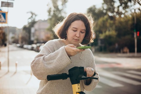 A woman scans a QR code on an electric scooter using her smartphone for easy rental in a sunny