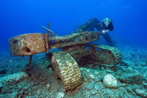 Diver looks at illuminated for diver sunken wreck of excavator tracked vehicle, Tenerife, Canary