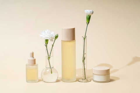 Minimalist arrangement of skincare dropper bottle, toner, and cream jar with white carnations in