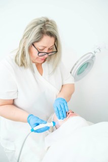 A professional cosmetologist uses a blue LED device for hydro-peeling on a client, targeting acne