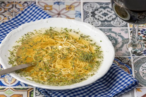 Noodle soup with herbs in a white plate next to a glass of red wine