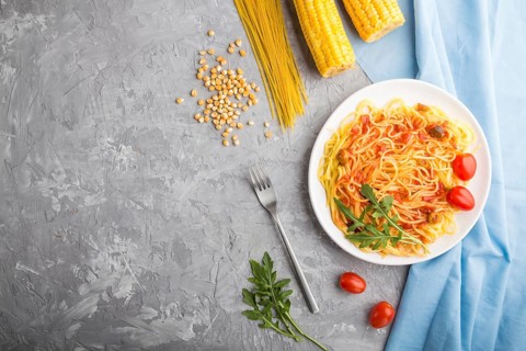 Corn noodles with tomato sauce and arugula on a gray concrete background and blue textile. Top