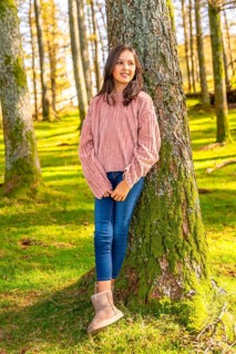 Vertical full length portrait of a cute teen girl leaning on tree trunk in an alpine forest