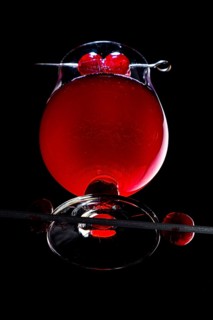 A cognac glass with red liquid and cherries, dramatically illuminated, view from below