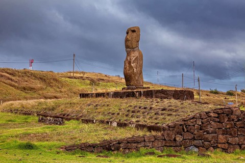 A single moai stands on a stone pedestal under a cloudy sky, the moai statues on Easter Island in