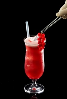 Red cocktail on ice cube cubes against a black background, red currants as garnish, studio