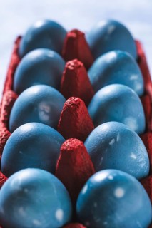 Vibrant blue Easter eggs neatly arranged in a bold red egg carton, shot from above. The contrasting