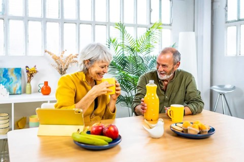 Happy senior woman having breakfast at home sharing and using digital tablet