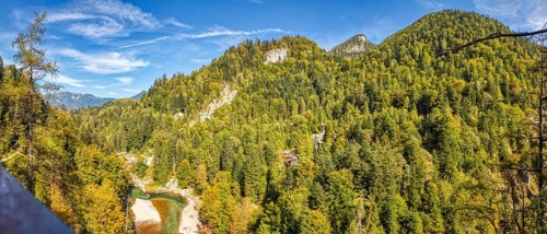 An expansive mountain panorama with densely wooded slopes under a clear blue sky, Klobenstein