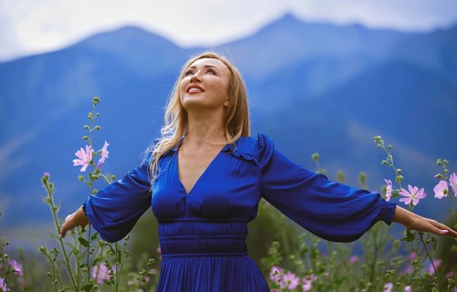 A joyful blond woman in a blue dress enjoys a moment of freedom surrounded by a vibrant grassy