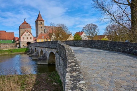 Paving stone road leads over stone bridge to a village with a characteristic church, spring,