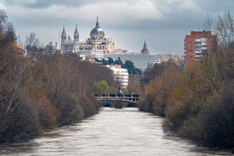 Captivating view of the Manzanares river flowing through Madrid, flanked by leafless trees. The
