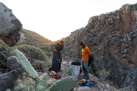 Climbers prepare their gear at sunset in a rugged natural landscape, surrounded by rocky cliffs and