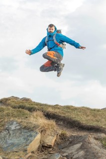 A man in vibrant outdoor gear joyfully leaps during a trekking adventure in the Pyrenees. The image