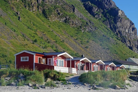 Red holiday cabins on the beach in front of green mountains on a sunny day, nature scenery,