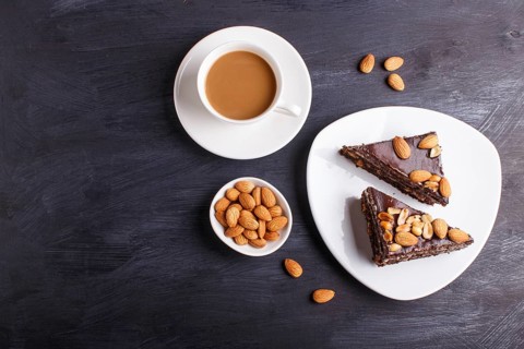 Chocolate cake with caramel, peanuts and almonds on a black wooden background. cup of coffee, top