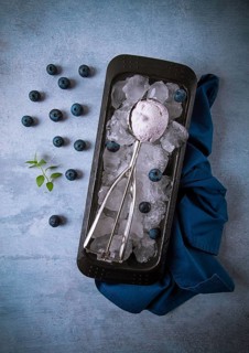 Blueberry ice cream, container with a spoon, on a gray table, fresh blueberries