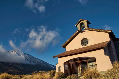 Ermita de las Nieves, small building in front of a snow-covered mountain landscape under clear sky,