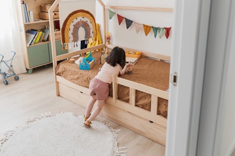 A young girl plays in a cozy, colorful bedroom with a wooden bed and playful decorations,