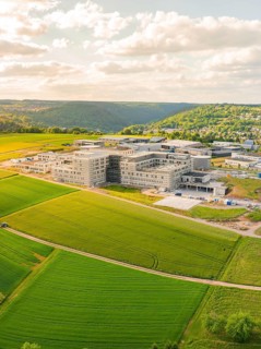 Aerial view of a large building complex surrounded by green fields and hills, construction of the