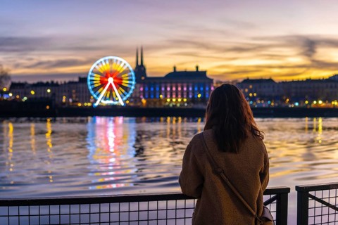 Young woman standing on a waterfront promenade, looking at the illuminated christmas ferris wheel