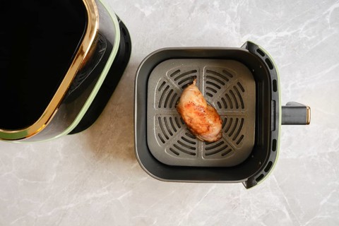 Top view of cooked chicken leg inside modern air fryer basket placed on marble countertop in home