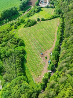 Aerial view of a solar park under construction, surrounded by green fields and forests in the rural