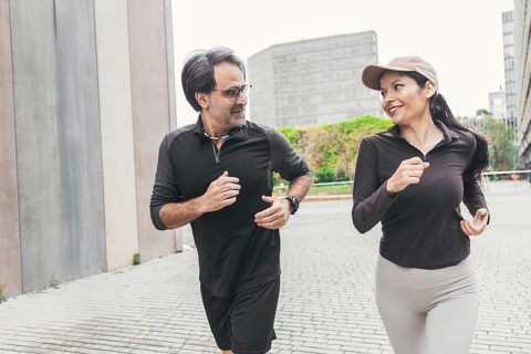 A joyful couple is jogging together on a city street, dressed in sportswear. They enjoy the