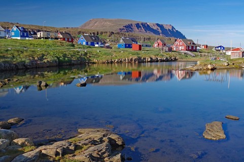 Colourful village reflected in calm water in front of high mountains